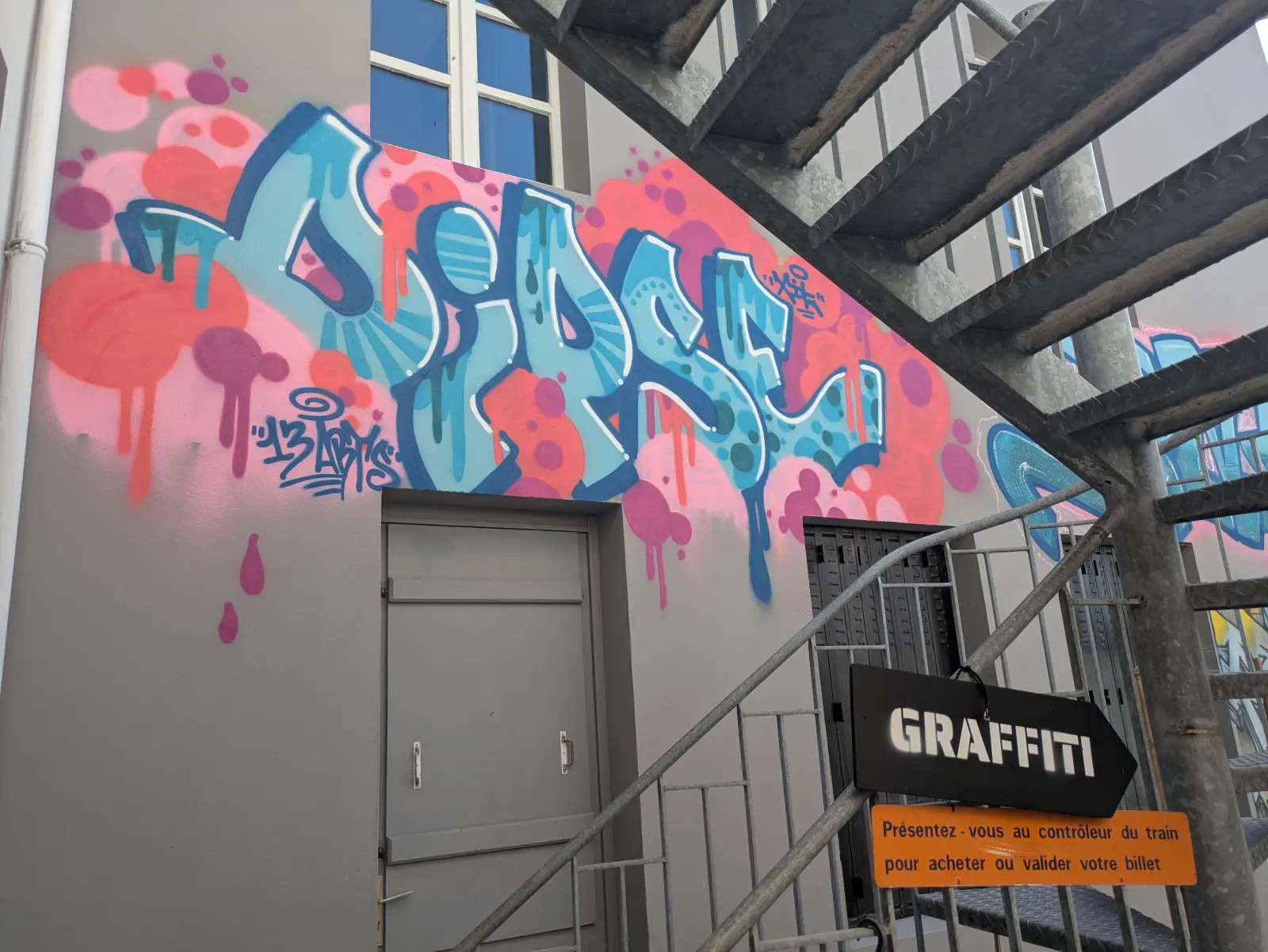 Graffiti coloré style street art sur façade intérieure avec escalier métallique, visible dans les locaux de l’association 13 Arts – espace dédié au graffiti et aux arts urbains