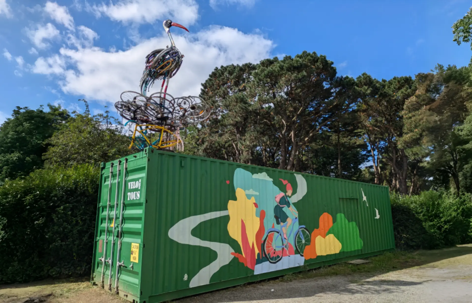 oiseau en structure métalique sur un conteneur avec une peinture muticouleur d'une femme a velo
